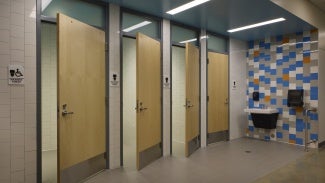hallway with entry to 4 single-user bathrooms, and external sink near them